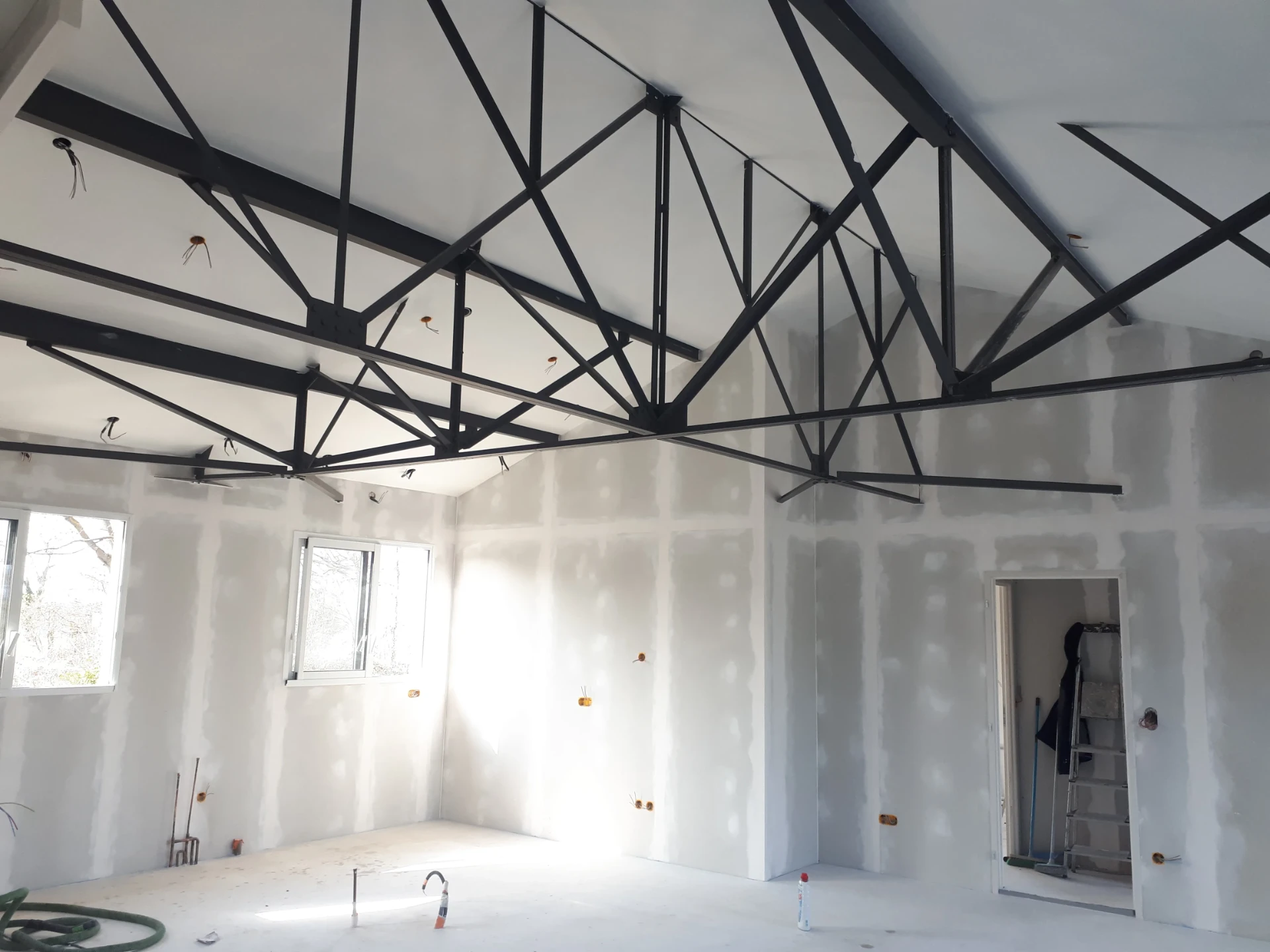 Chantier de placoplâtre sous une charpente métallique noire